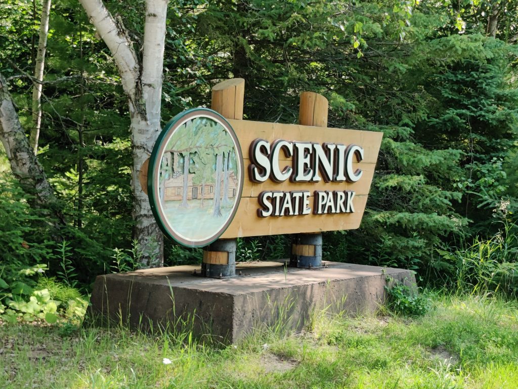 Brown wooden sign with white letters that read Scenic State Park at Scenic State Park in Bigfork, MN